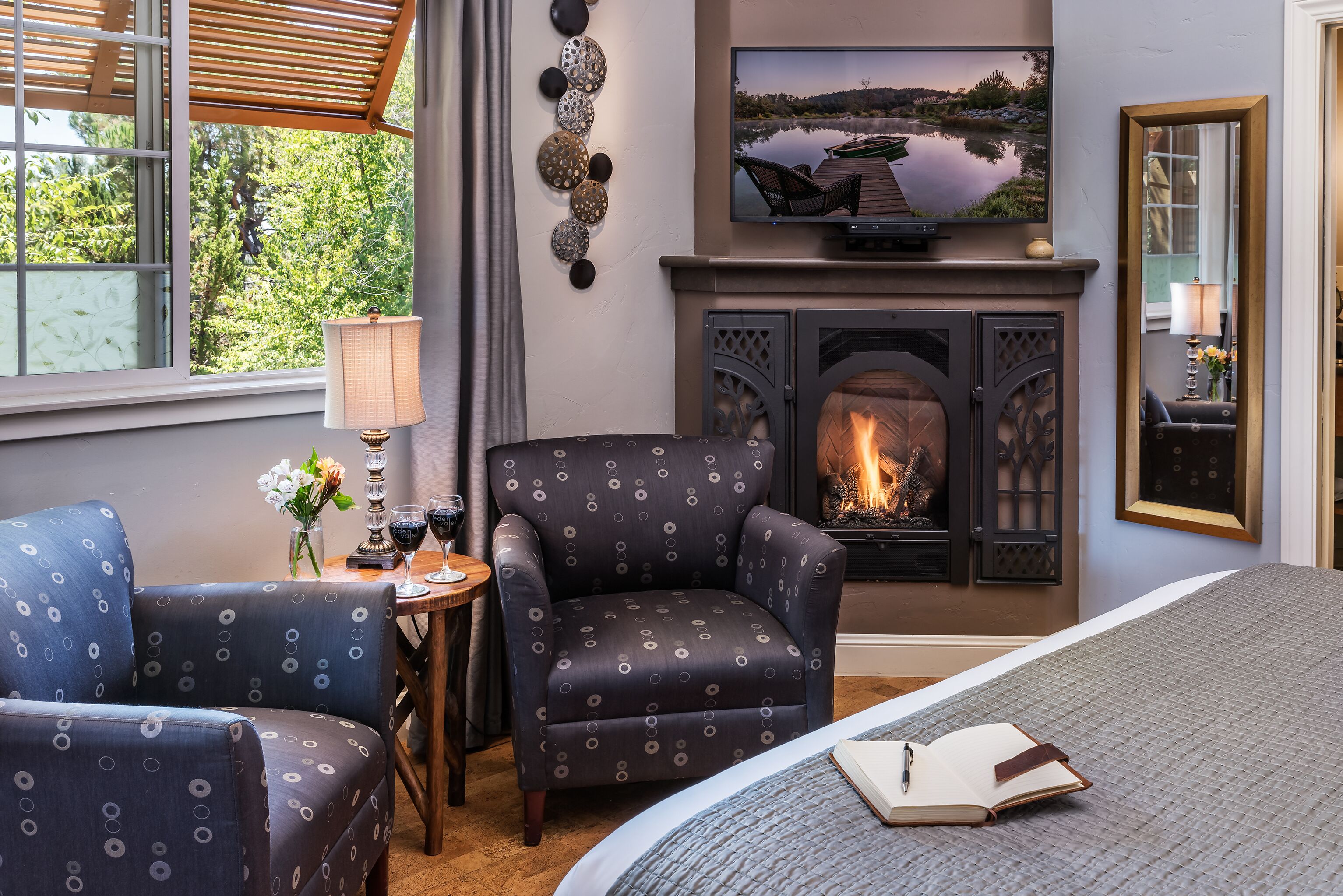 A cozy room with a fireplace, a comfortable armchair, a sofa, a TV, and a bed with an open book.