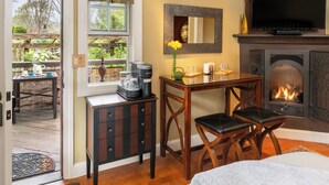 A cozy room with a fireplace, a dining table with chairs, a small cabinet, and a window with a view of the outdoors.