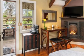 A cozy room with a fireplace, a dining table with chairs, a small cabinet, and a window with a view of the outdoors.