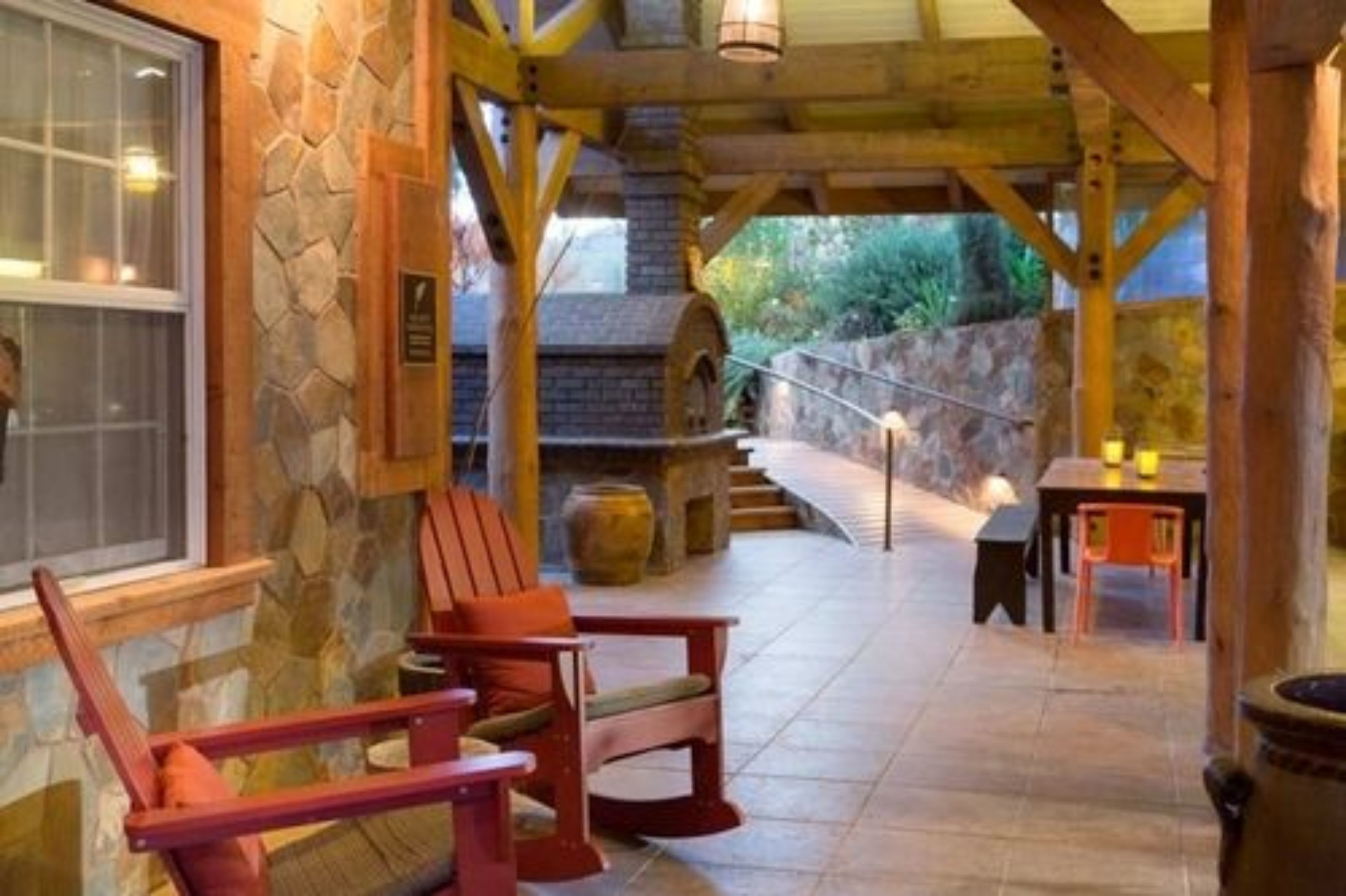 A stone-walled outdoor area with wooden beams, a stone fireplace, and a seating area with two Adirondack chairs.
