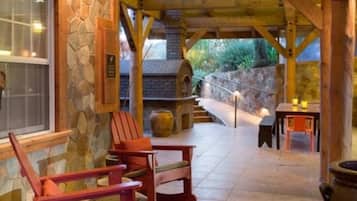 A stone-walled outdoor area with wooden beams, a stone fireplace, and a seating area with two Adirondack chairs.