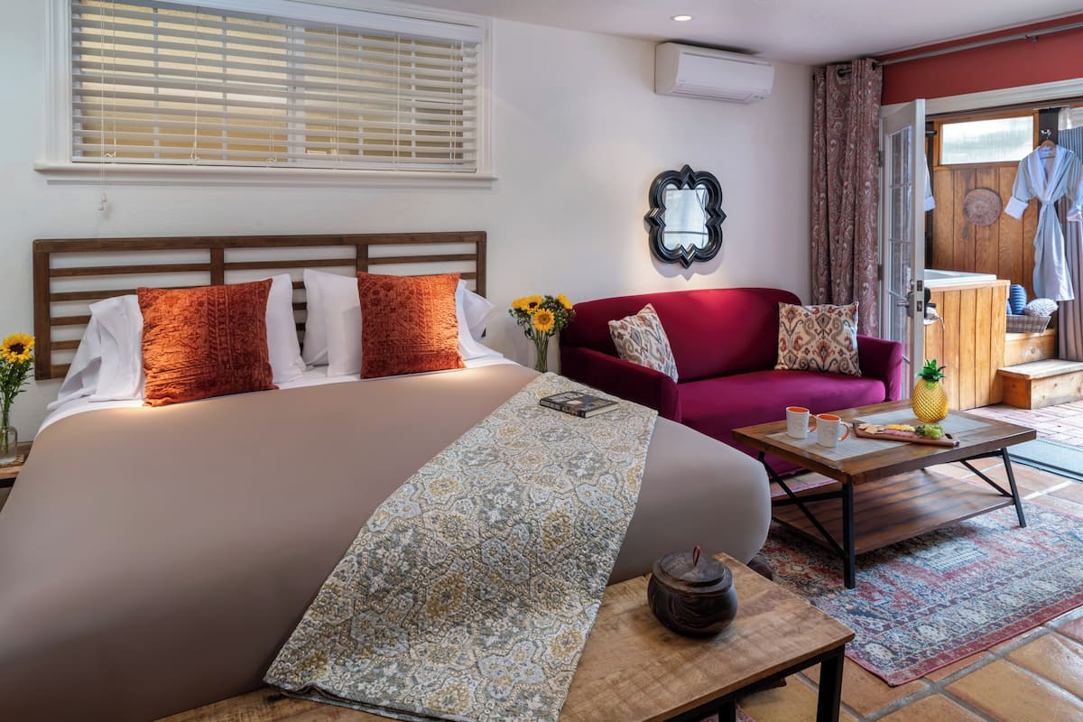 A hotel room with a large bed, a red sofa, a wooden coffee table, and a small table with a vase and a pineapple.