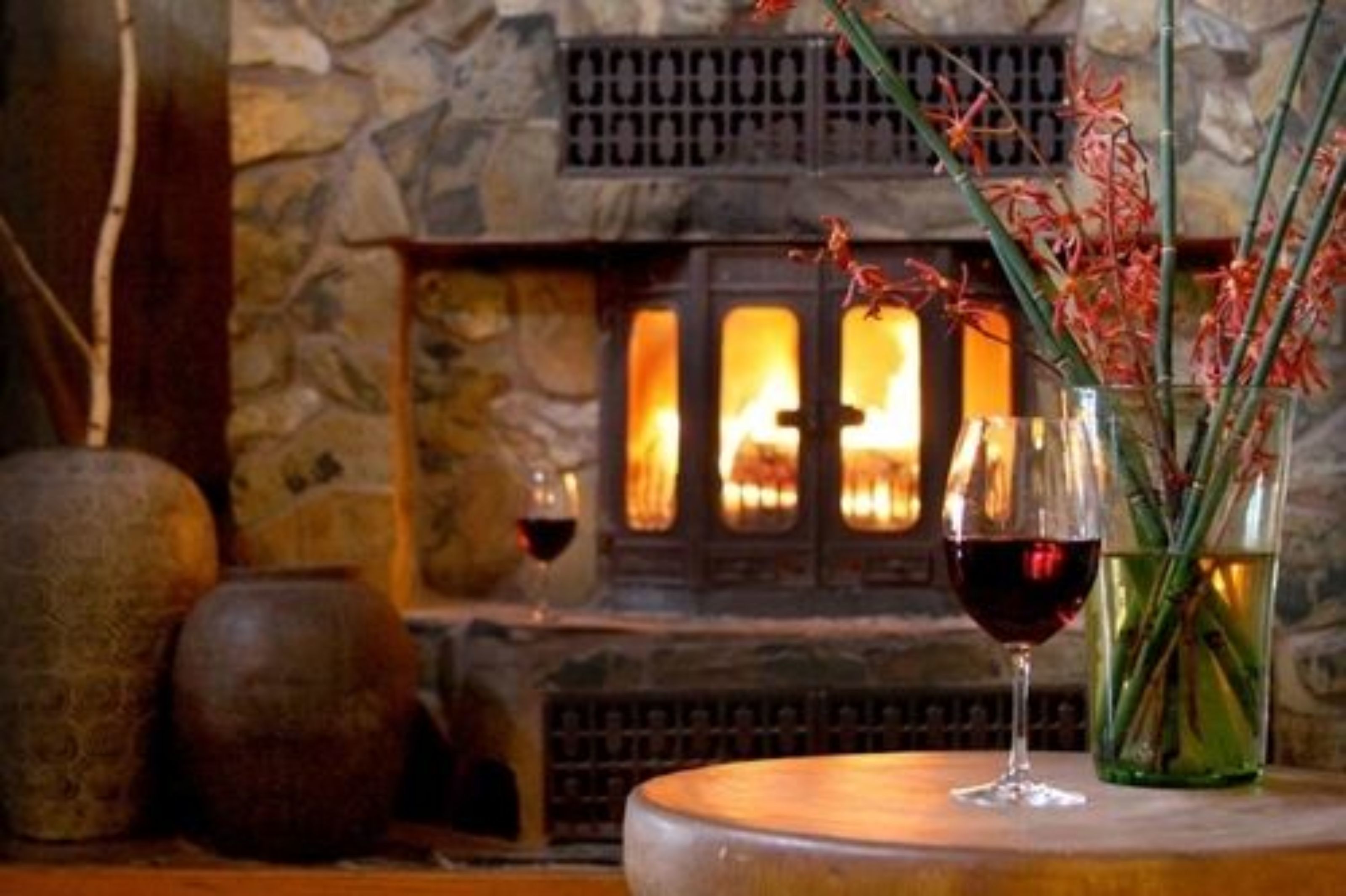 A cozy room with a stone fireplace, a glass of red wine, and decorative vases.