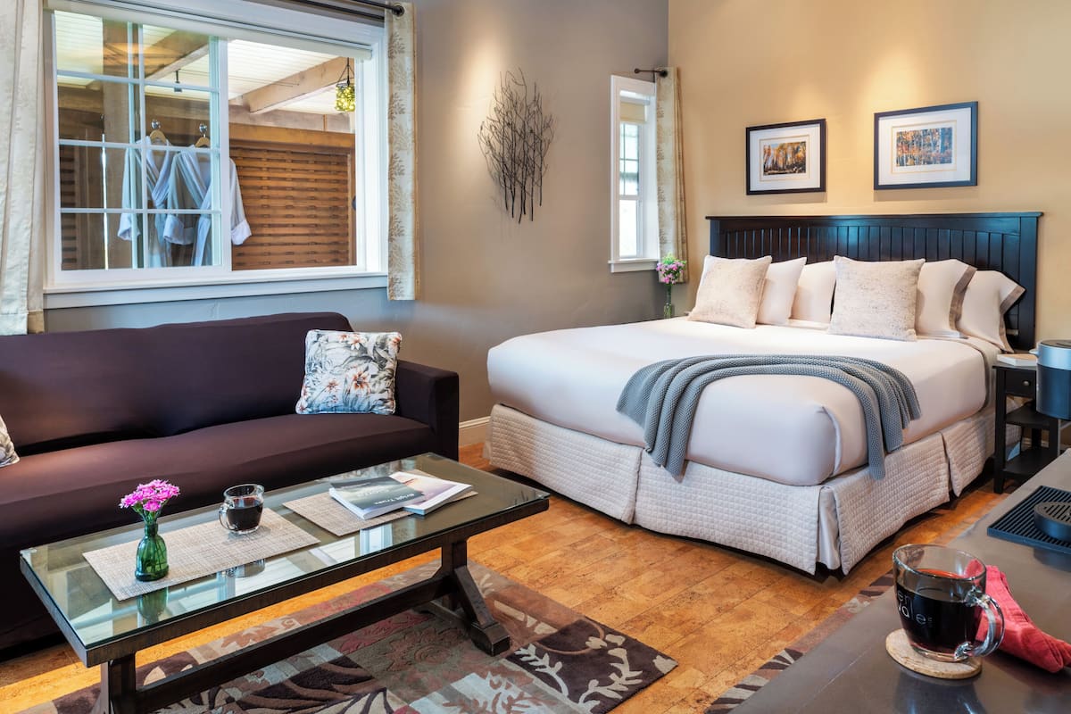 A hotel room with a bed, a sofa, a coffee table, and a window with curtains.