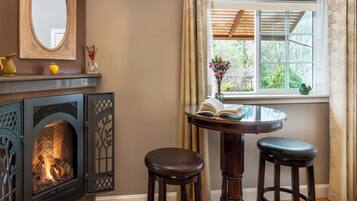 Una habitación acogedora con chimenea, una mesa redonda con dos taburetes, una ventana con vistas a la vegetación y un espejo en la pared.
