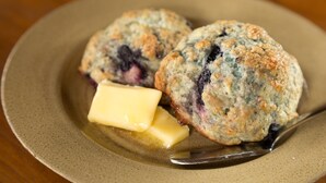 Two blueberry muffins on a plate with a piece of butter.