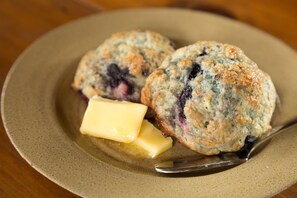 Two blueberry muffins on a plate with a piece of butter.