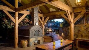 An outdoor wooden structure with a stone fireplace, a wooden table, and a bench.