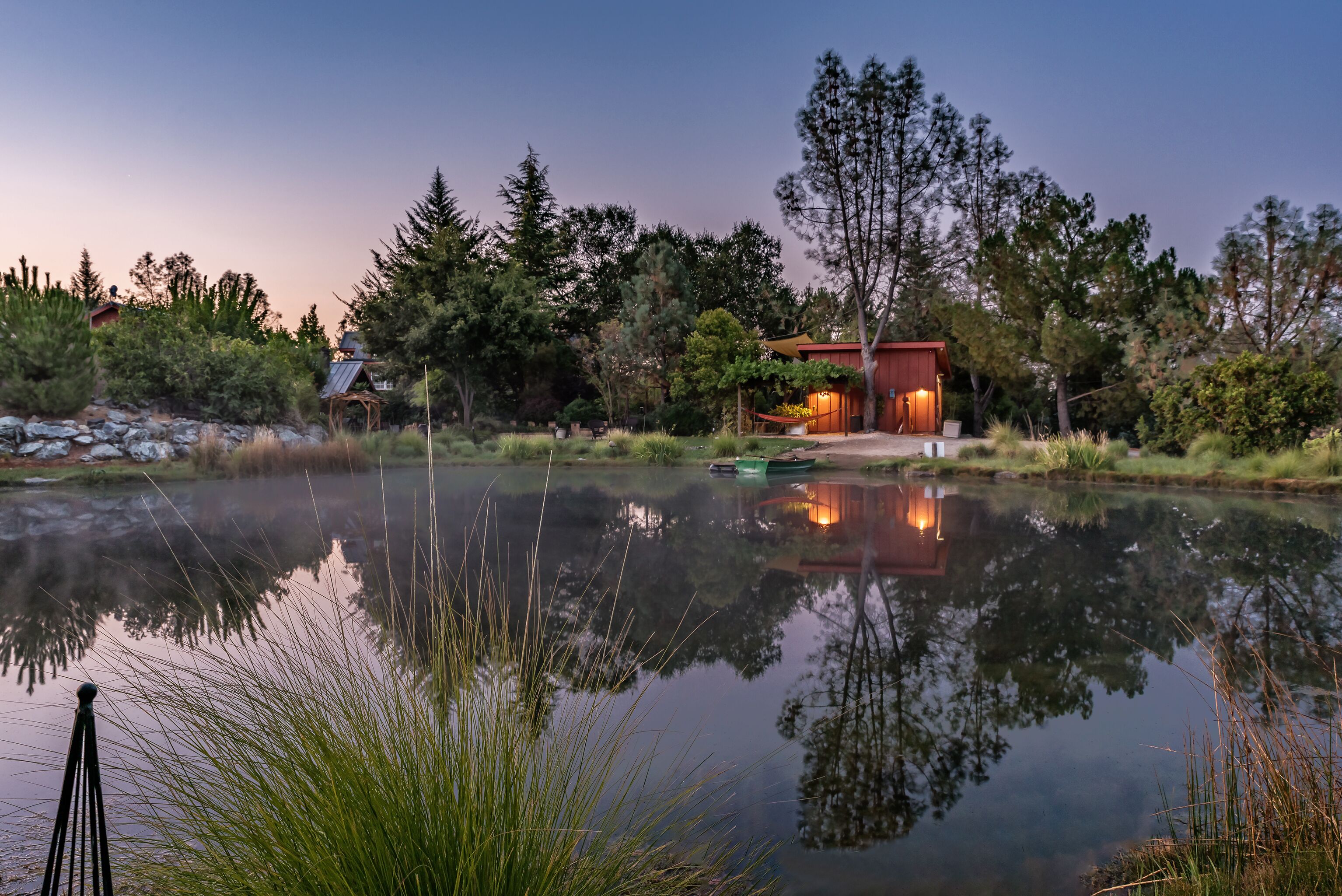 A lakeside cabin with a reflection in the water, surrounded by trees and a small dock.