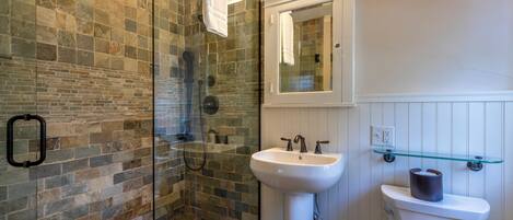 A bathroom with a glass shower enclosure, a white sink, and a toilet.