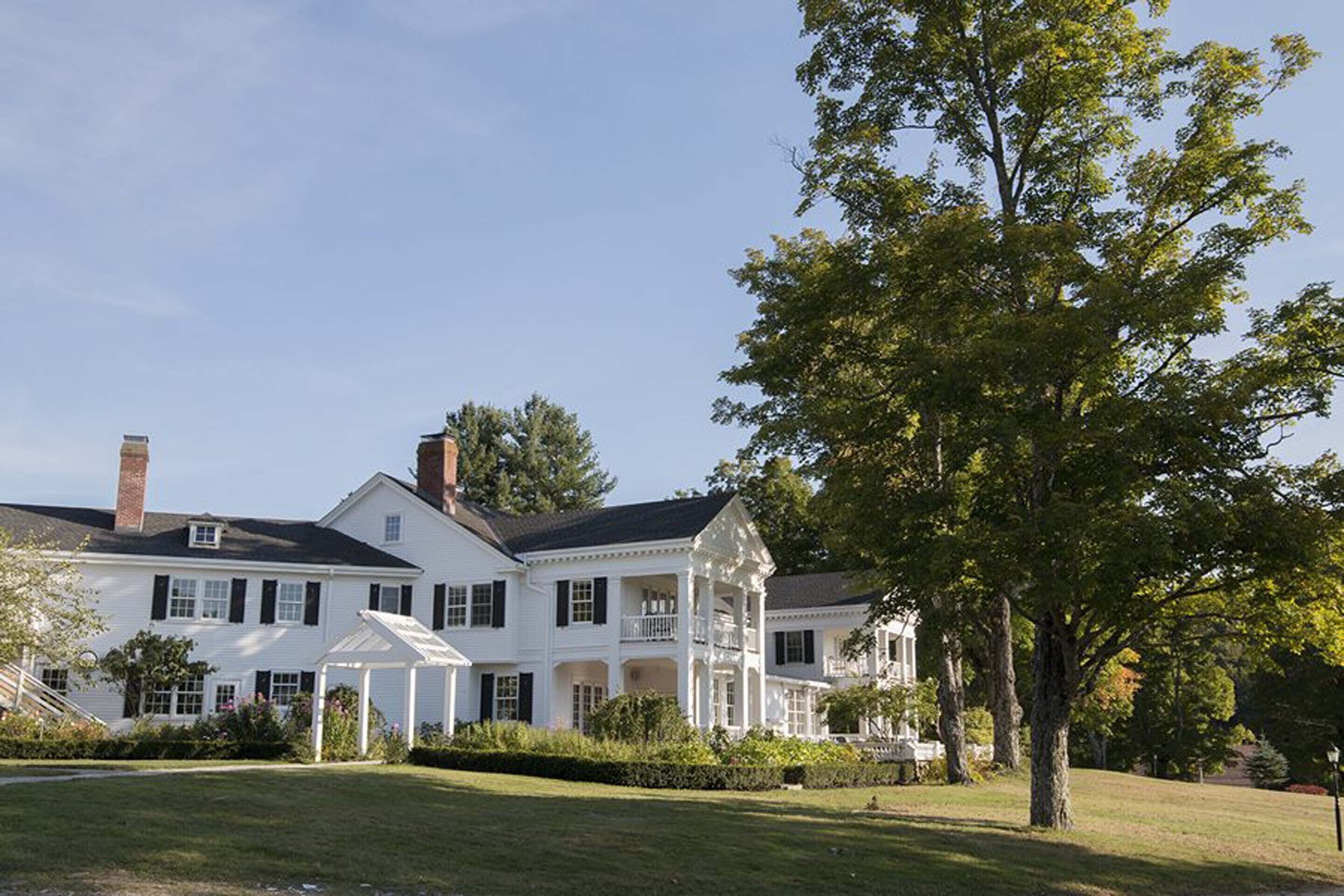 A large, white colonial-style house with multiple stories, a covered porch, and a well-maintained lawn.