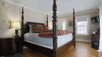 A four-poster bed with a dark finish, a bedside table with a lamp, a clock, and a dresser with a television on top.