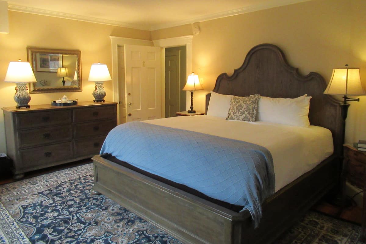 Quarto com uma cama grande, duas mesas de cabeceira com luminárias, um penteado e um espelho, além de uma porta.