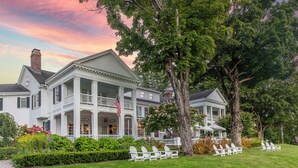 A large, white colonial-style house with a porch, surrounded by lush greenery and trees. - The White House Inn (Wilmington)