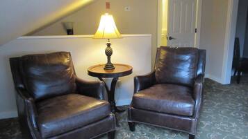 A room with two leather armchairs, a small round table with a lamp, and a patterned carpet.
