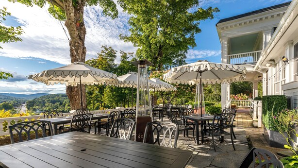 Eine Außenpatio mit Tischen, Stühlen, Sonnenschirmen und Blick auf die Landschaft.