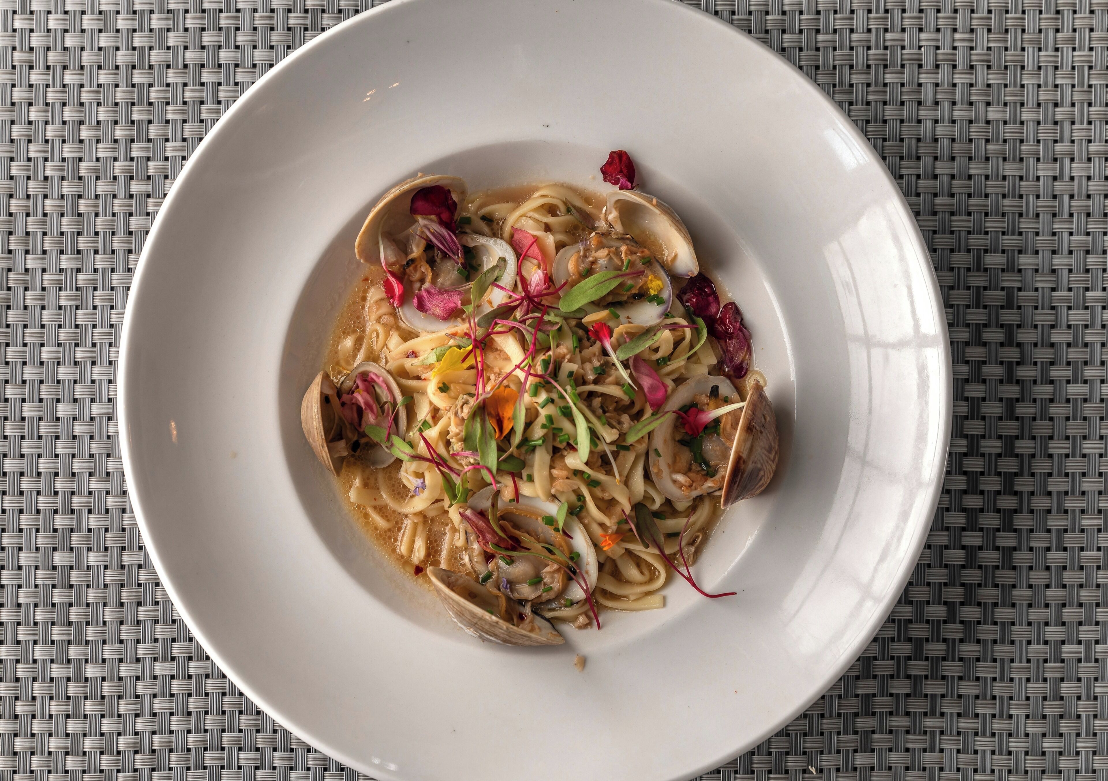 Un plato de pasta con almejas y verduras sobre un mantel tejido.