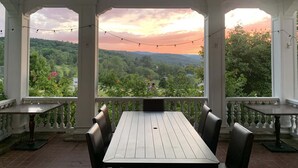Eine überdachte Terrasse mit Tisch und Stühlen, die einen schönen Ausblick auf eine Landschaft mit Bäumen und Hügeln bietet.