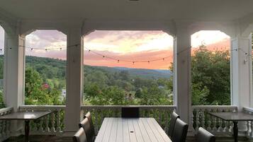 Un patio techado con una mesa y sillas, con vistas a un paisaje pintoresco con árboles y colinas.