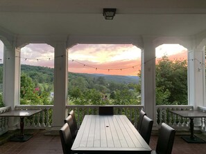 A covered patio with a table and chairs, overlooking a scenic landscape with trees and hills.