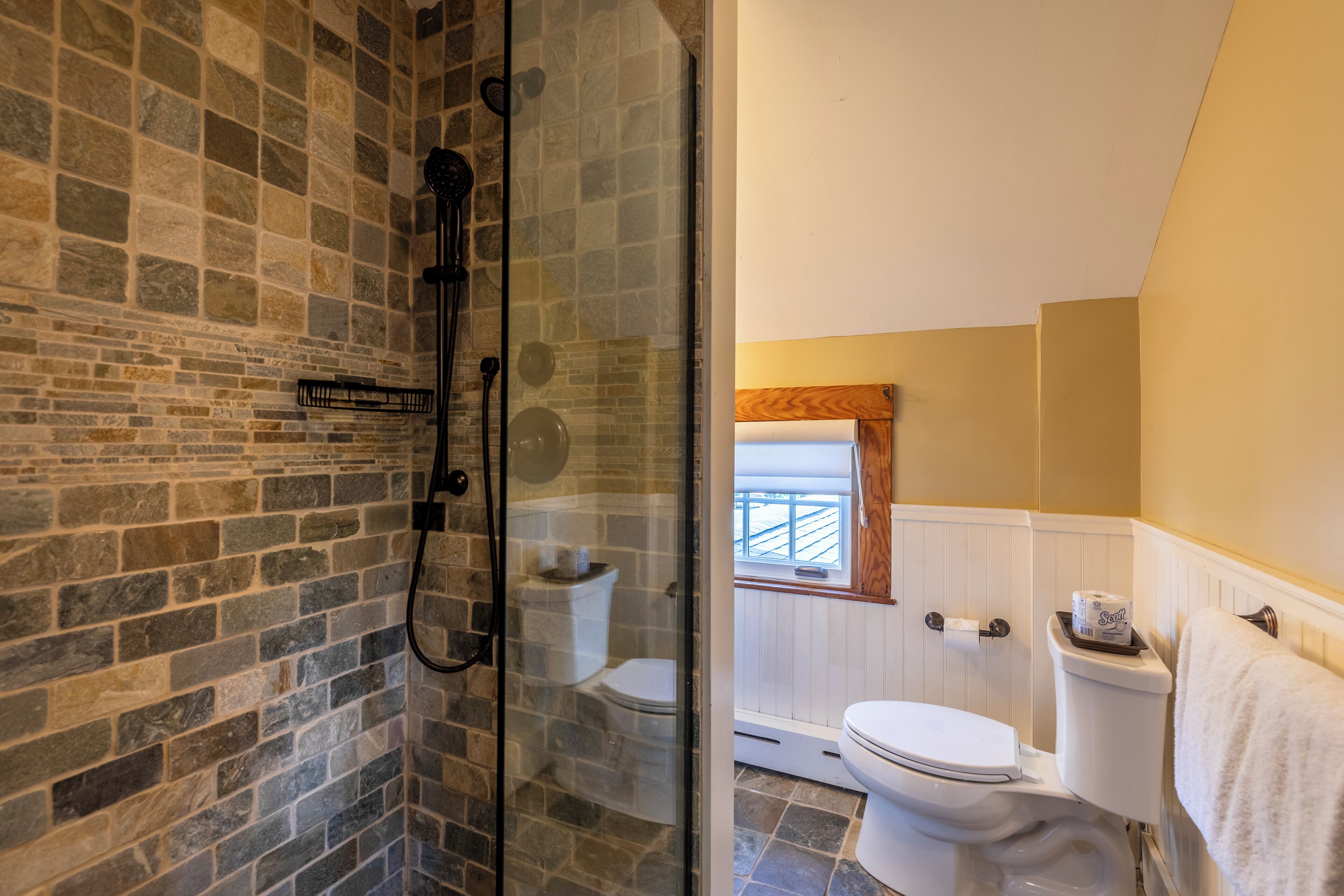 Un baño con cabina de ducha de piedra, inodoro y ventana con vistas.