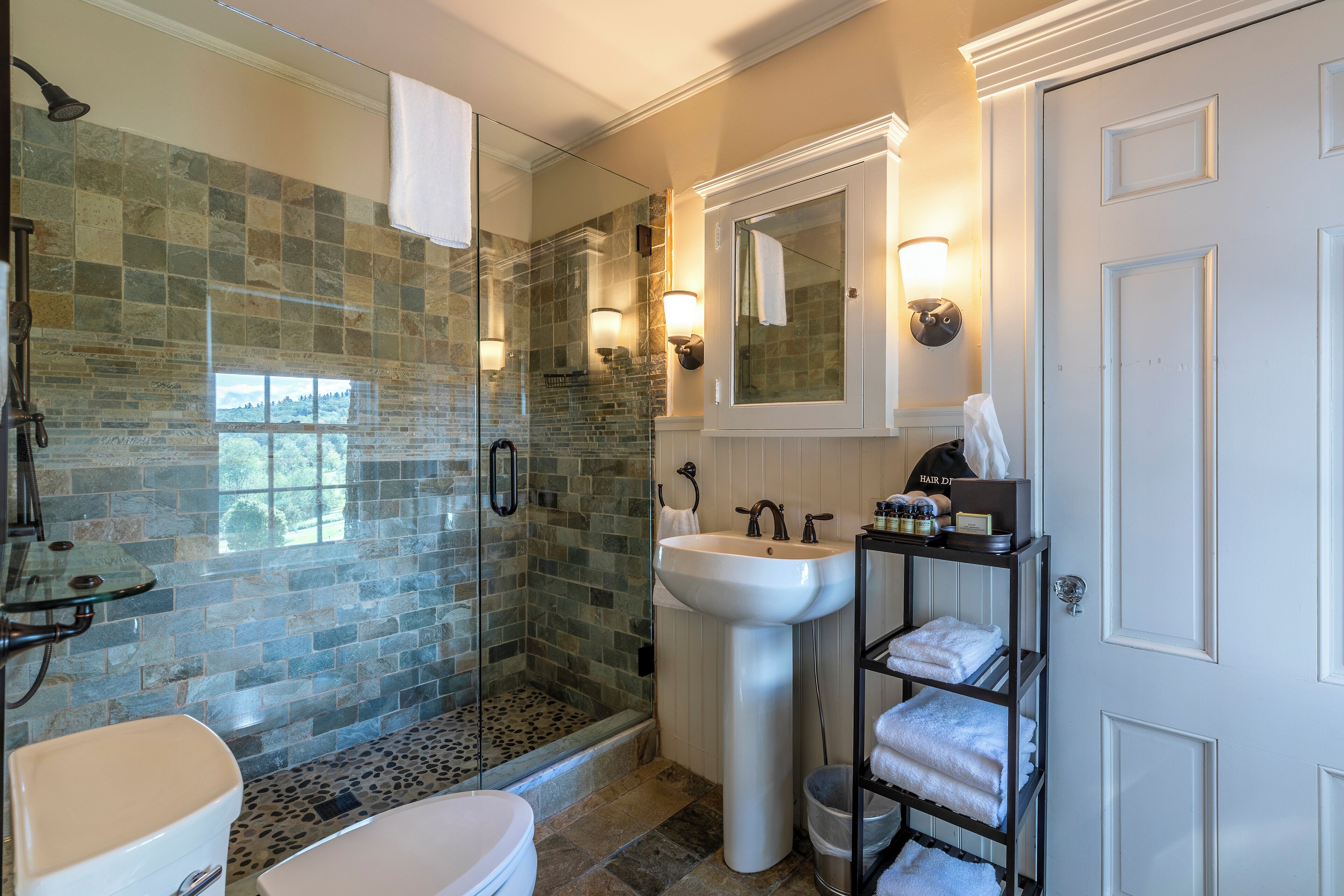 A bathroom with a glass shower enclosure, a white sink, and a towel rack with towels.