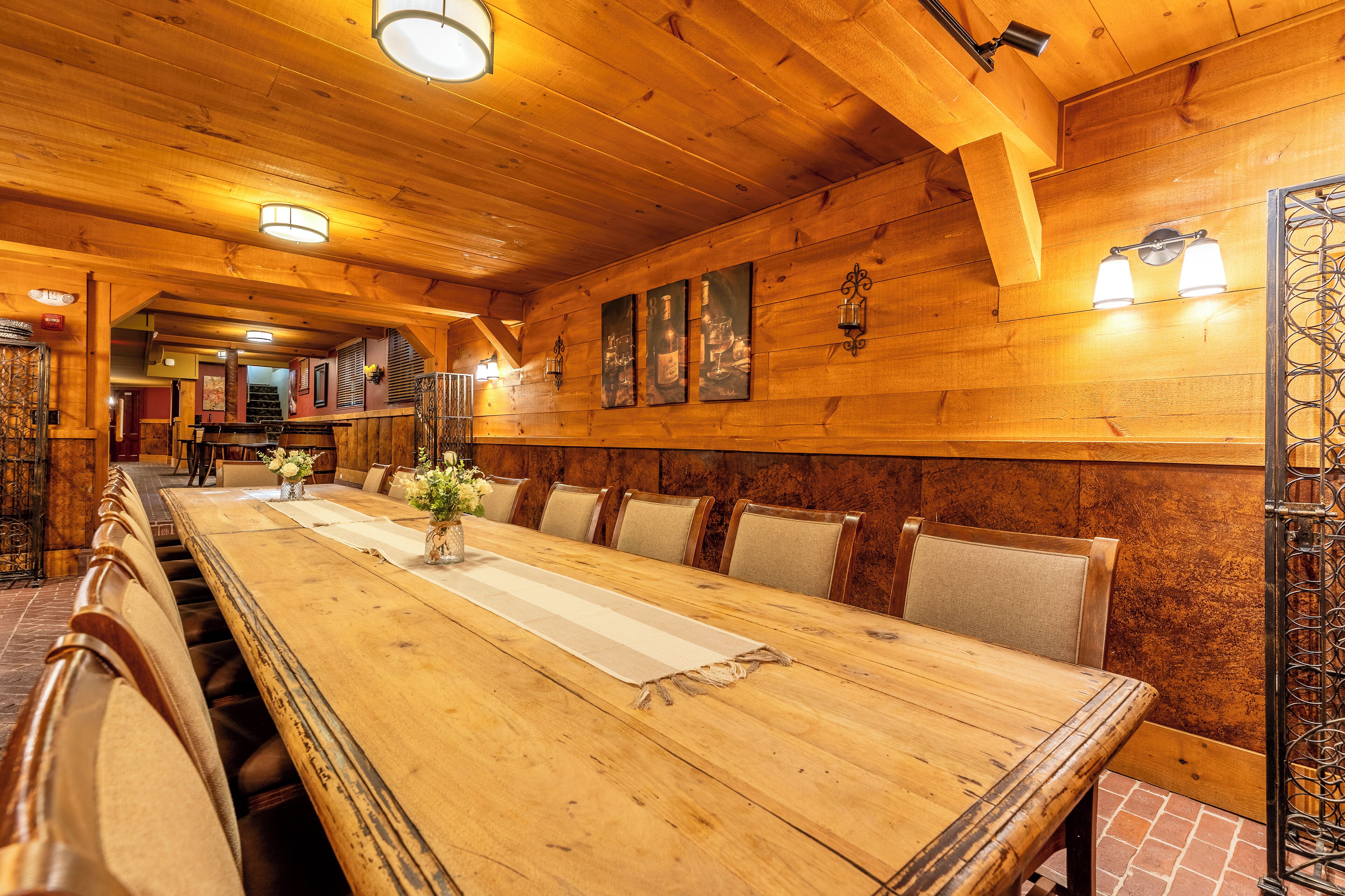 Una larga mesa de comedor de madera con sillas acolchadas, paredes de madera e iluminación instalada en la pared.