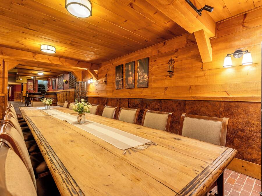 Una larga mesa de comedor de madera con sillas acolchadas, paredes de madera e iluminación instalada en la pared.