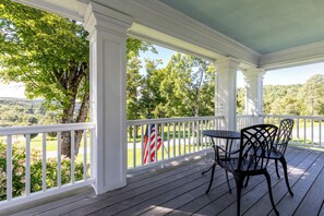 A covered porch with white railings, a table, and two chairs.