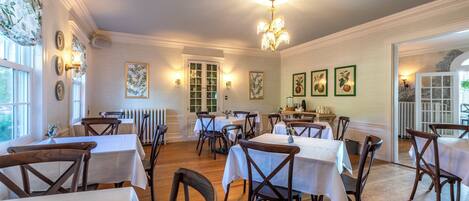 A dining area with multiple tables and chairs, a chandelier, and wall-mounted light fixtures.