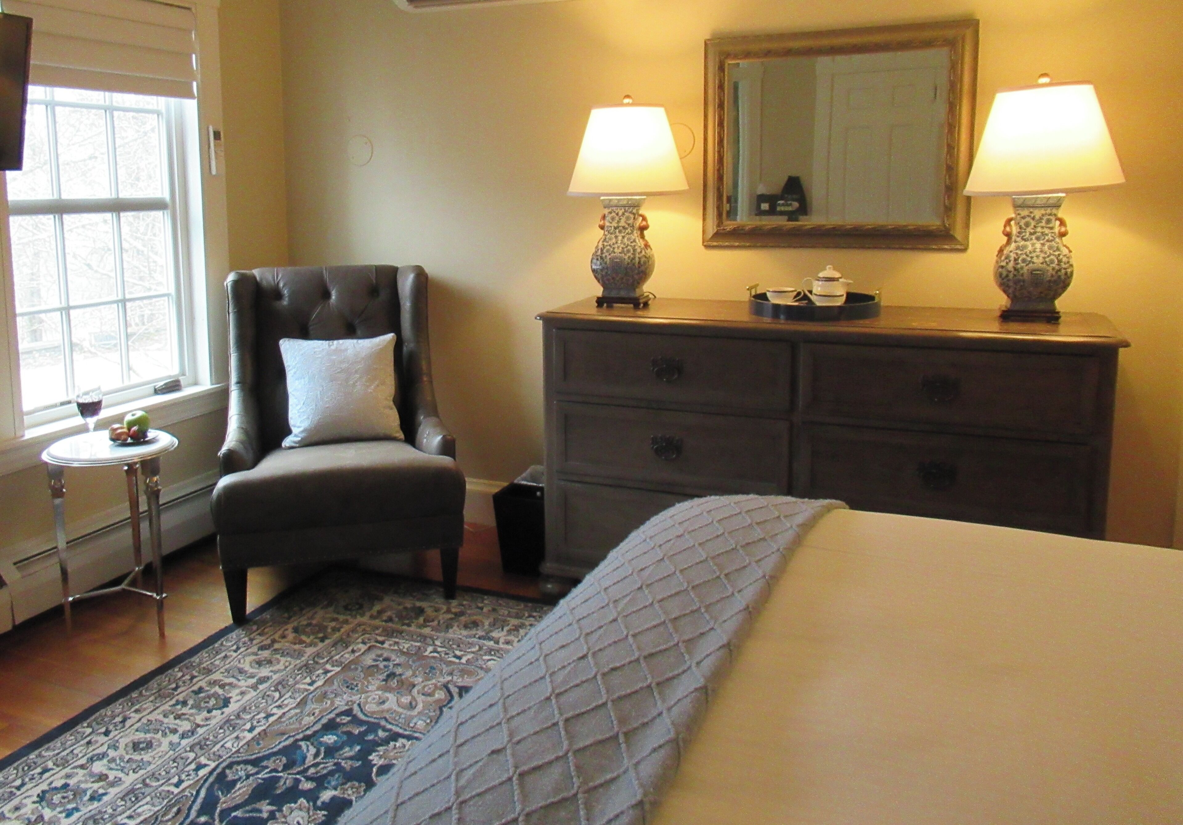A hotel room with a bed, a chair, a dresser, two lamps, a mirror, and a window with blinds.