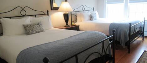 A double bed with a headboard, a bedside table with a lamp, and a window with blinds.