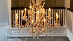 A grand chandelier with multiple candle-like lights, a white balustrade, and an arched doorway in the background. - The White House Inn (Wilmington)