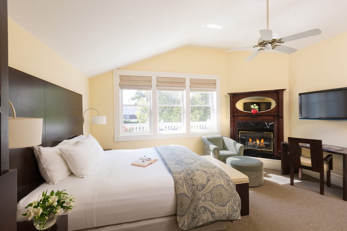 A hotel room with a large bed, a fireplace, a television, and a desk.