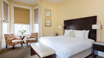 Una habitación de hotel con una cama grande, dos sillones, una mesita con un jarrón de flores y una mesita de noche con una lámpara.