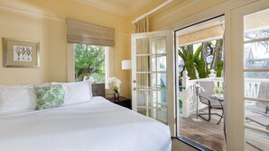 A hotel room with a large bed, a window with a view of greenery, a door leading to an outdoor balcony, and a framed botanical print on the wall. - Healdsburg Inn on the Plaza, A Four Sisters Inn (Healdsburg)