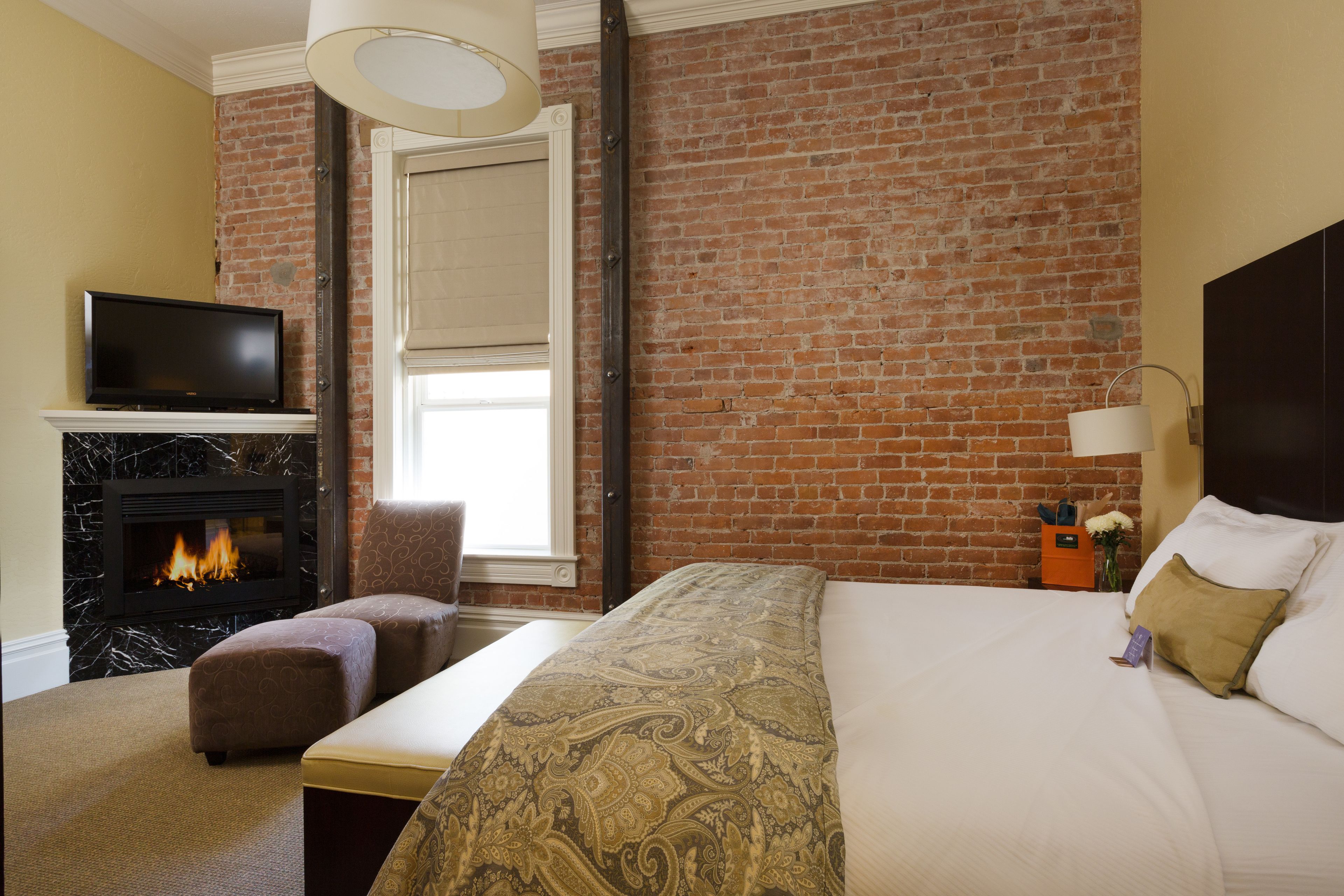 Une chambre d’hôtel avec un mur en briques, une cheminée, un lit et un téléviseur.
