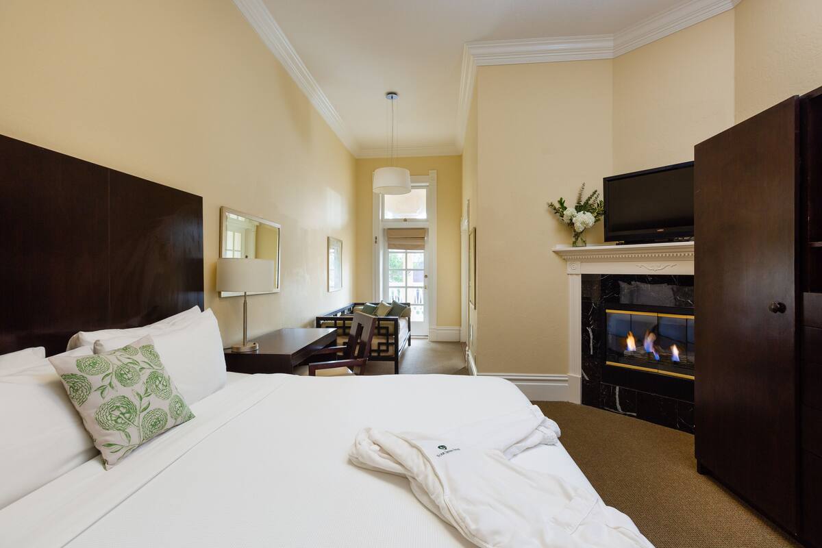 A hotel room with a large bed, a flat-screen TV, a fireplace, and a desk with a chair.