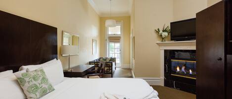 A hotel room with a large bed, a flat-screen TV, a fireplace, and a desk with a chair.