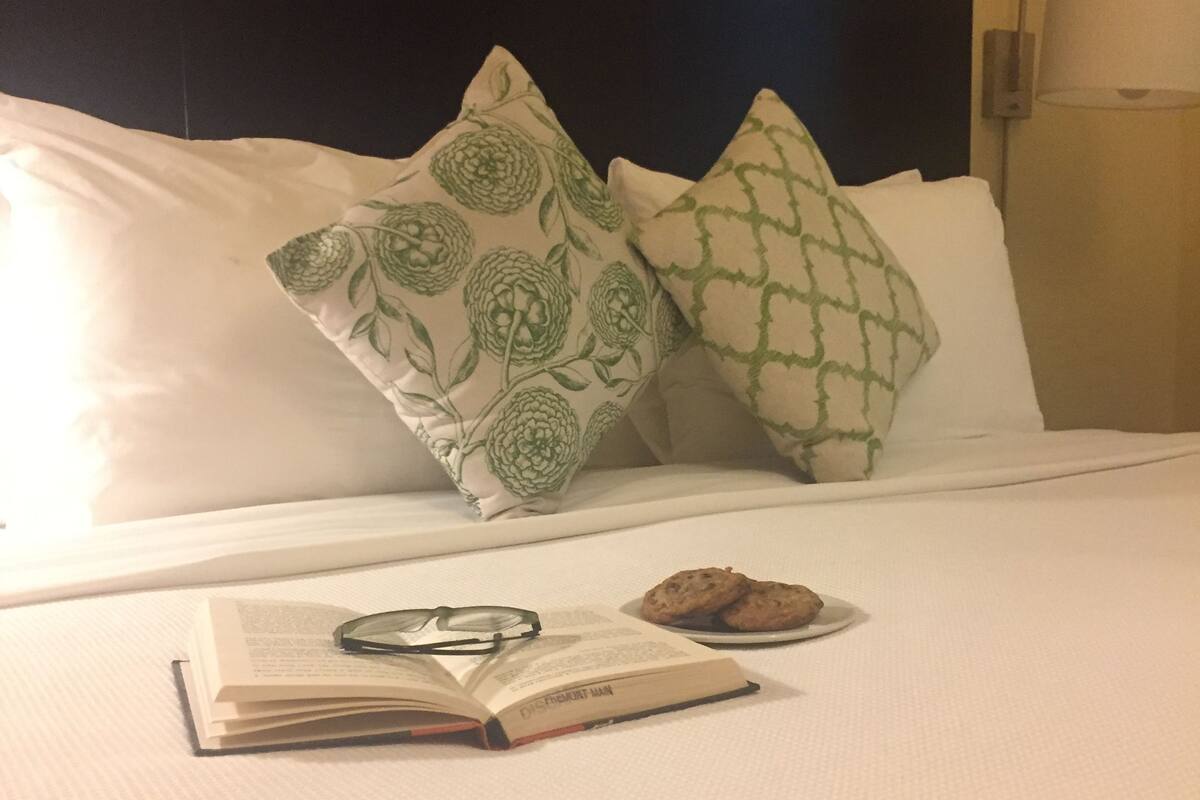 A neatly made bed with a book, glasses, and cookies on the bed.