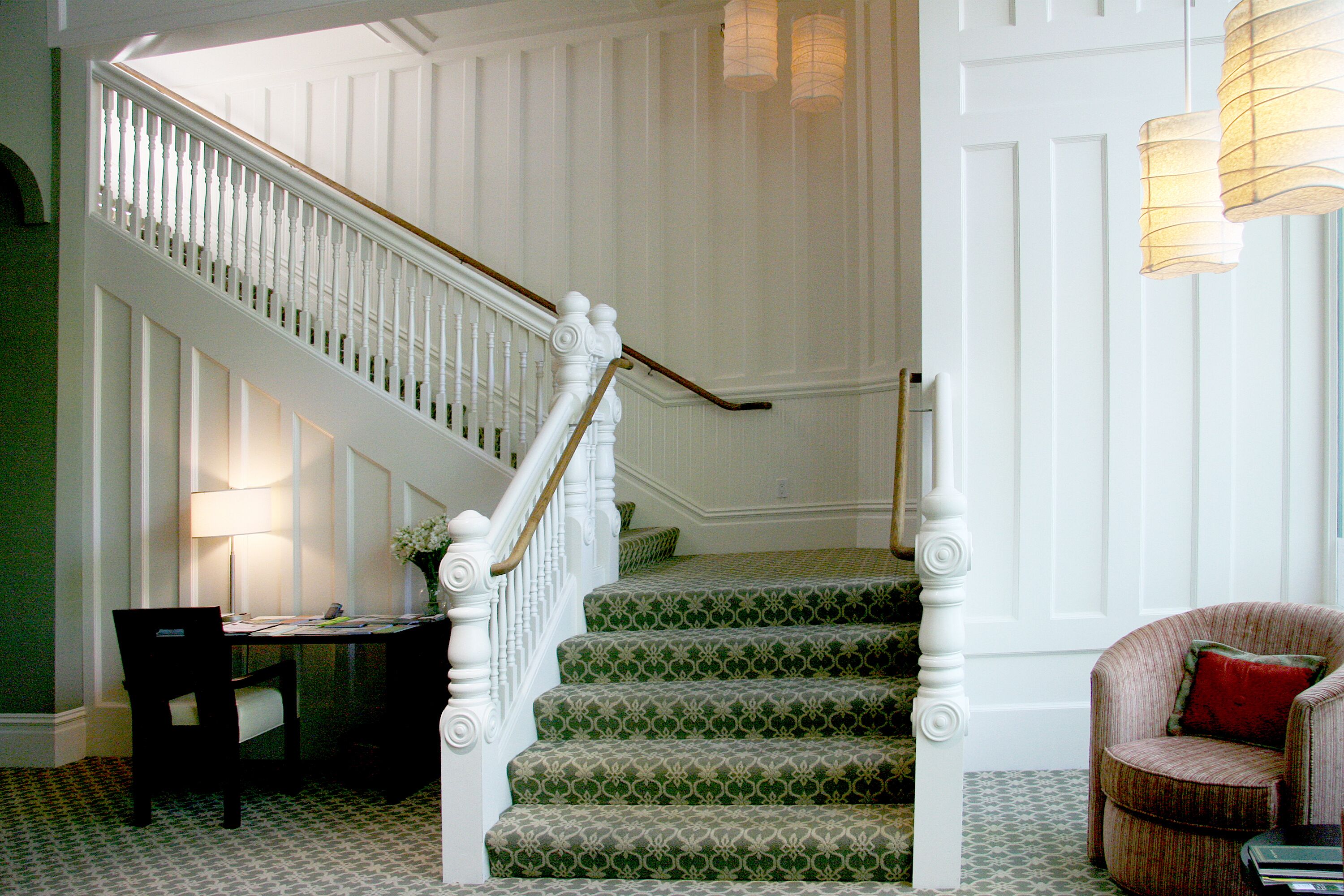 A staircase with white balusters and green patterned carpet leading to a landing.