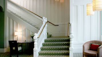 A staircase with white balusters and green patterned carpet leading to a landing.
