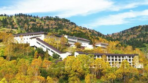 A hillside building complex with multiple structures, surrounded by autumn foliage. - Manza Prince Hotel (Tsumagoi)