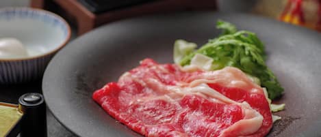 Primer plano de carne cruda en un plato, con un tazón y un recipiente pequeño al fondo.