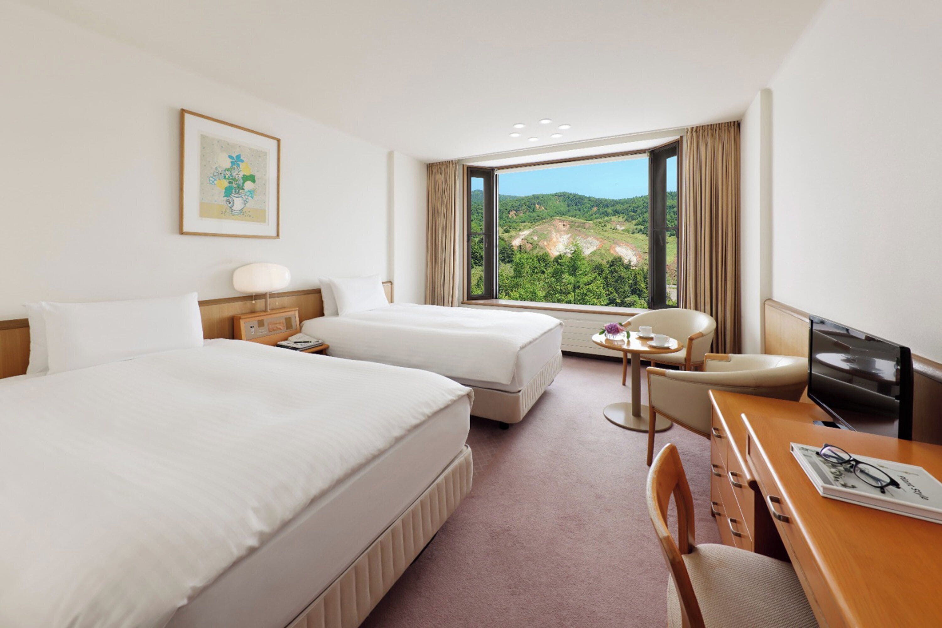 Habitación de hotel con dos camas, un escritorio, una silla, un televisor y una ventana con vistas a zonas verdes.
