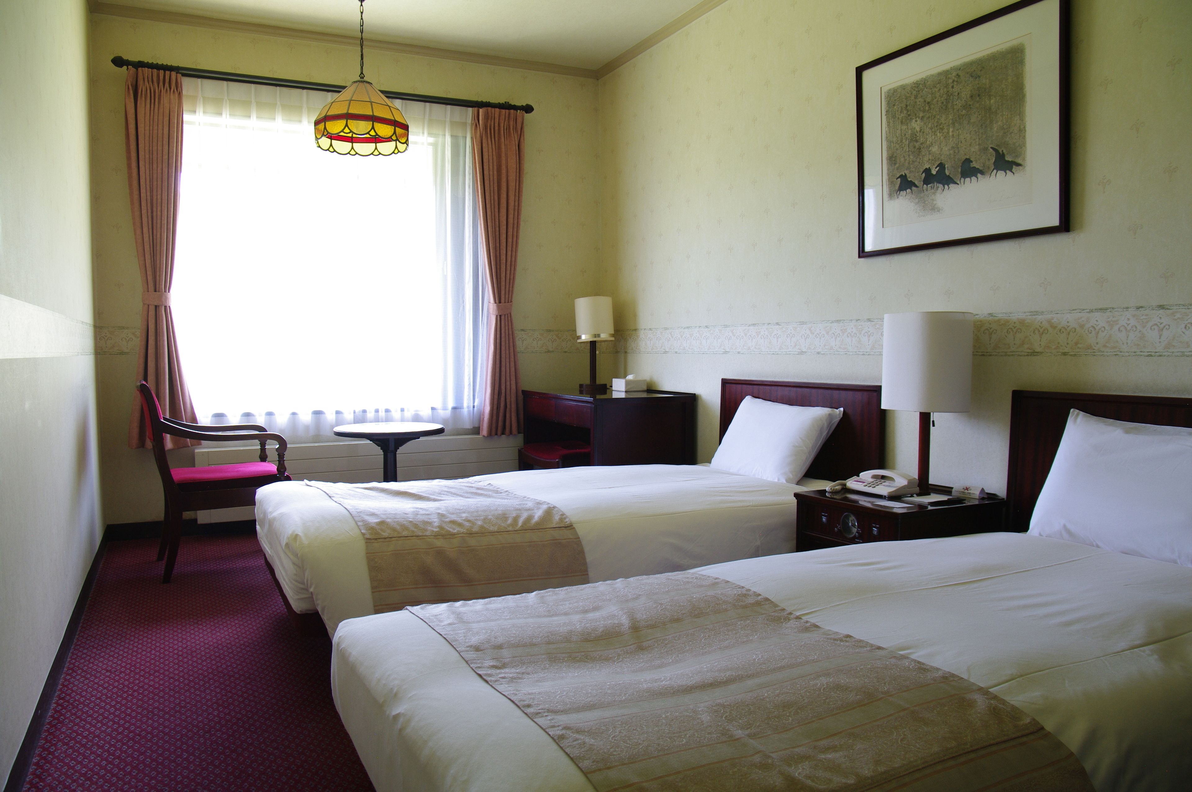 A hotel room with two beds, a chair, a desk, and a window with curtains.