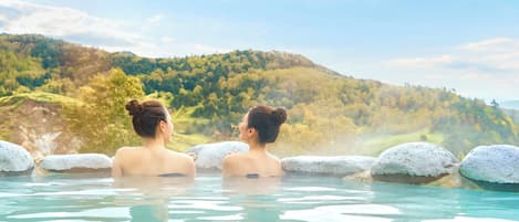 Two people in a hot spring with a mountainous backdrop.