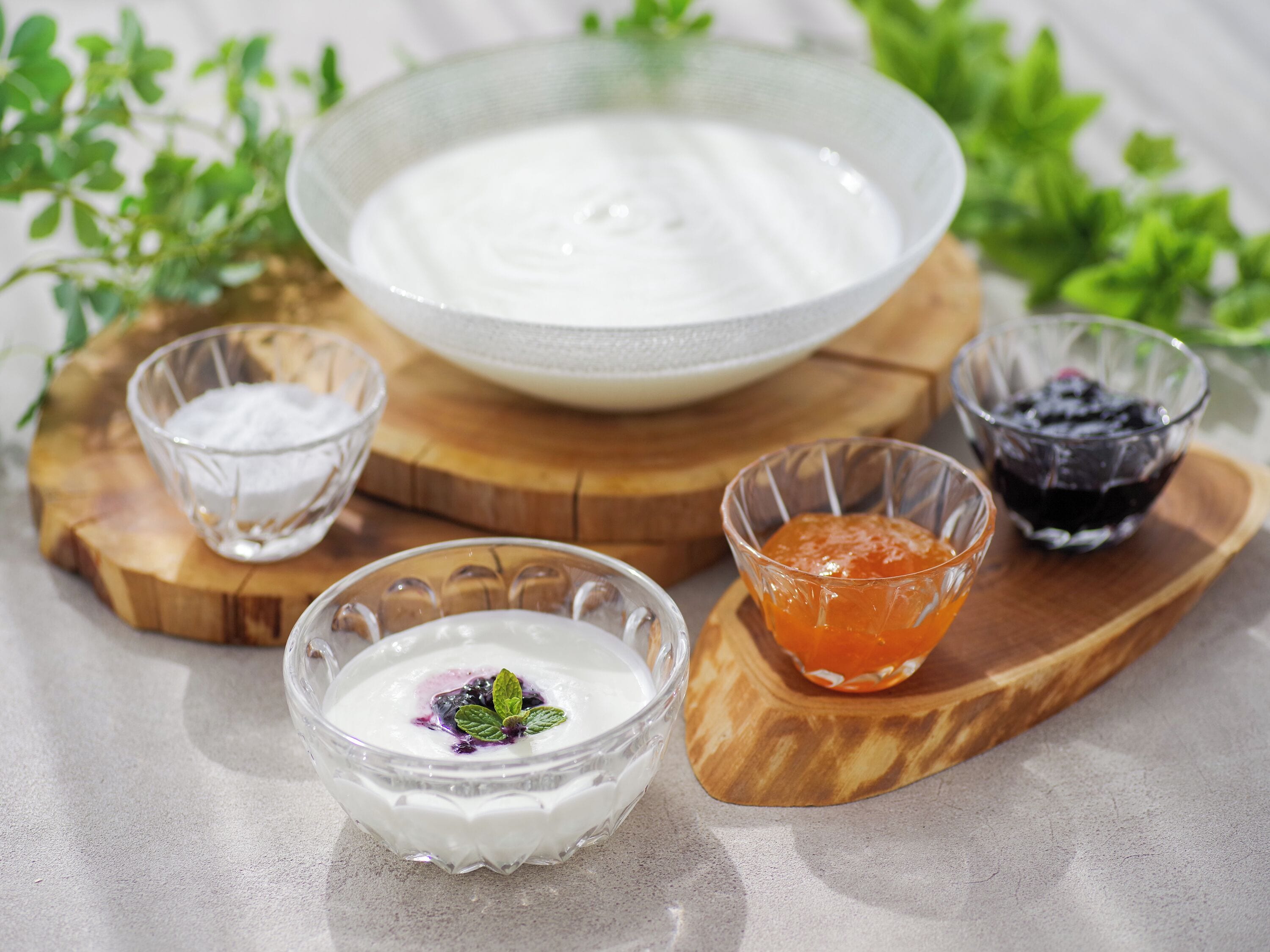 A bowl of white yogurt with a blueberry compote on a wooden board, accompanied by a glass of white yogurt and a glass of orange compote.
