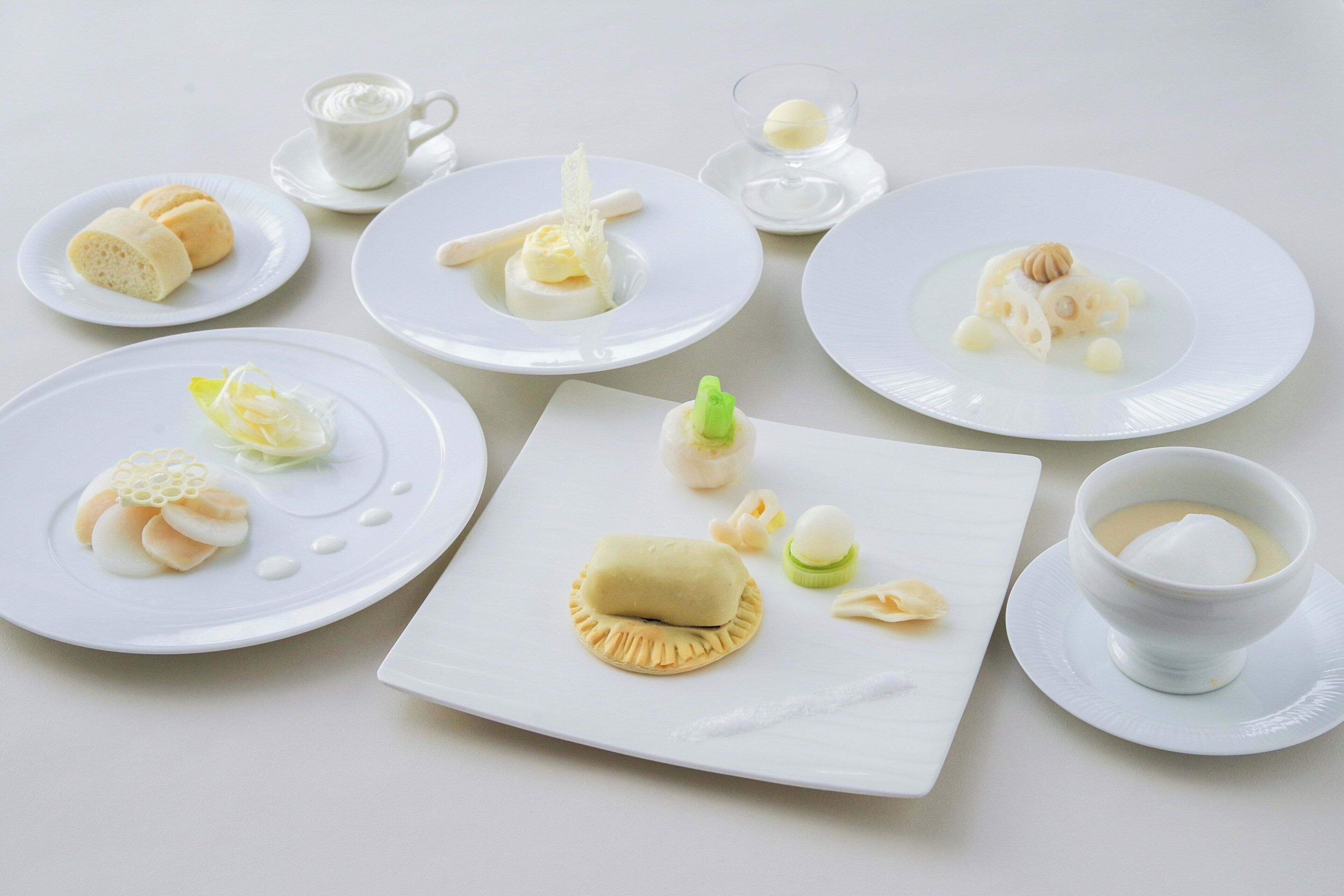 A table with various white plates and bowls containing food items.
