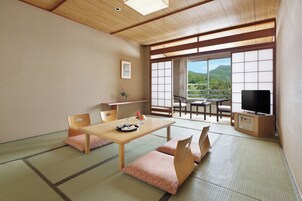 Una habitación japonesa tradicional con suelo de tatami, una mesa baja con cojines, un televisor y vistas a un paisaje montañoso a través de amplios ventanales.